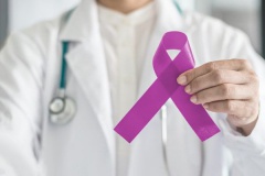 Far away blurry doctor with in-focus hand holding a purple ribbon